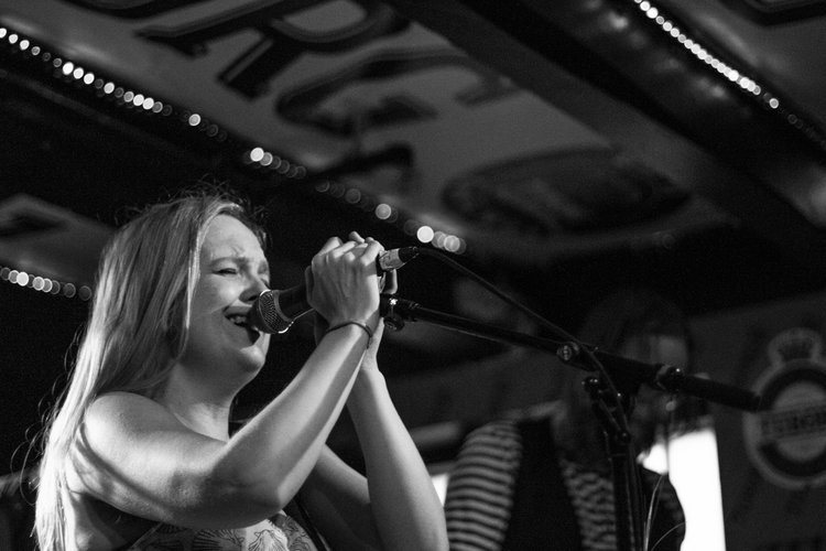 A woman singing into a microphone on stage in a black and white photo.