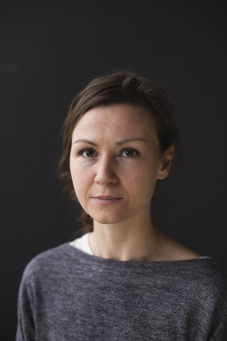 Portrait of a woman with short brown hair wearing a gray sweater against a black background.