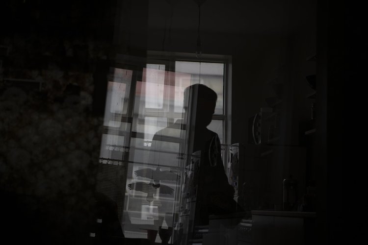 A dark interior scene with a person silhouetted near a window, with reflections of outdoor elements visible on the glass, including an eagle mural and building structures.