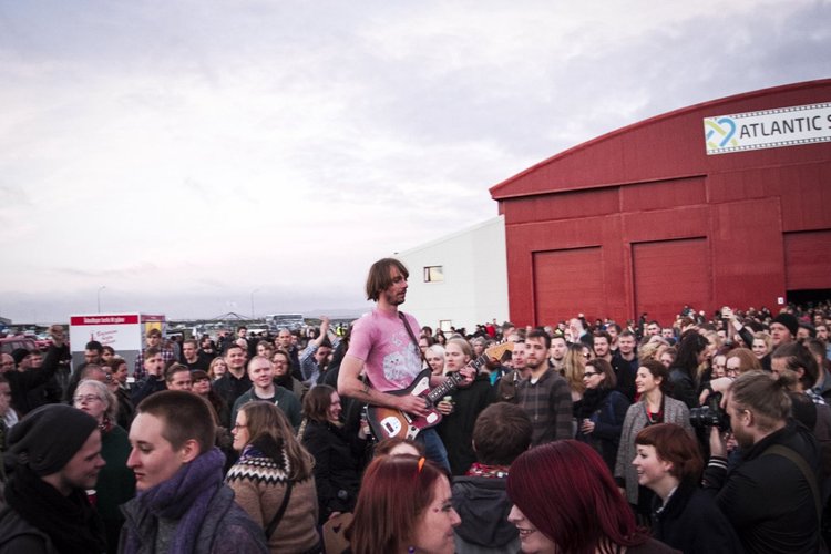 Crowd gathered outside a red building with a man playing an electric guitar in the center.