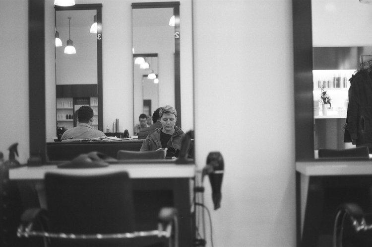 People sitting at tables in a modern cafe with hanging light fixtures, seen through a doorway or mirror.