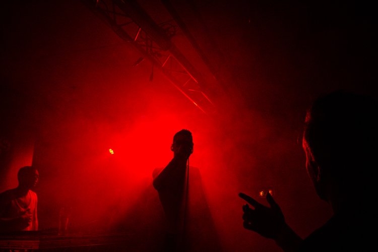Silhouettes of people on a stage illuminated by red lighting, likely during a concert or performance.