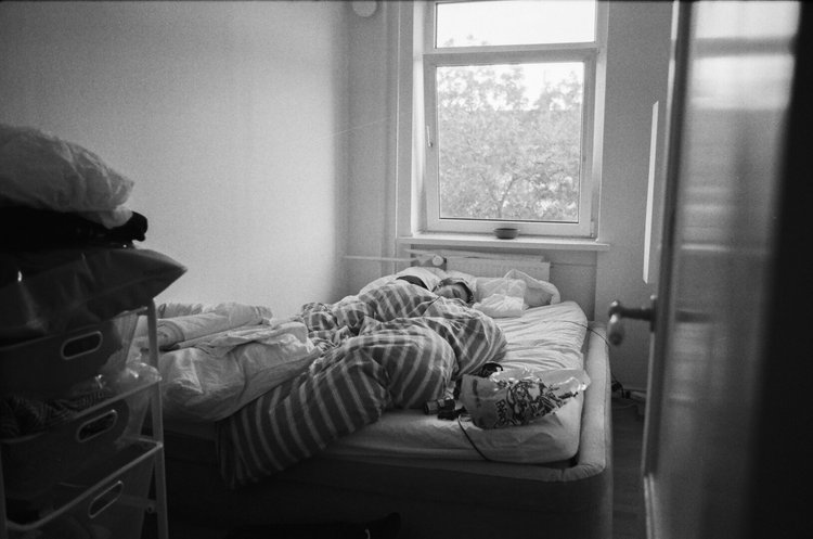 A person sleeping on a bed in a bedroom with an open window showing trees outside.