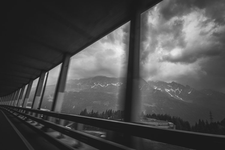 Black and white photo of a mountain landscape viewed through a bus window with a barrier and support beams.