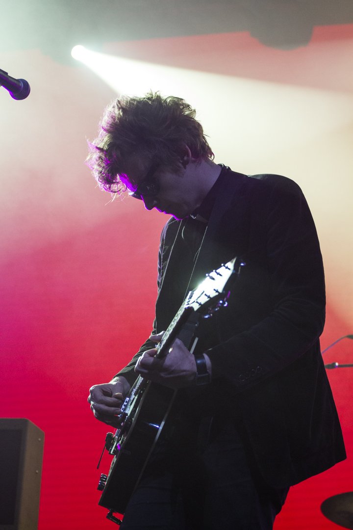 A musician playing an acoustic guitar on stage, backlit with colorful stage lights, creating a silhouette effect.