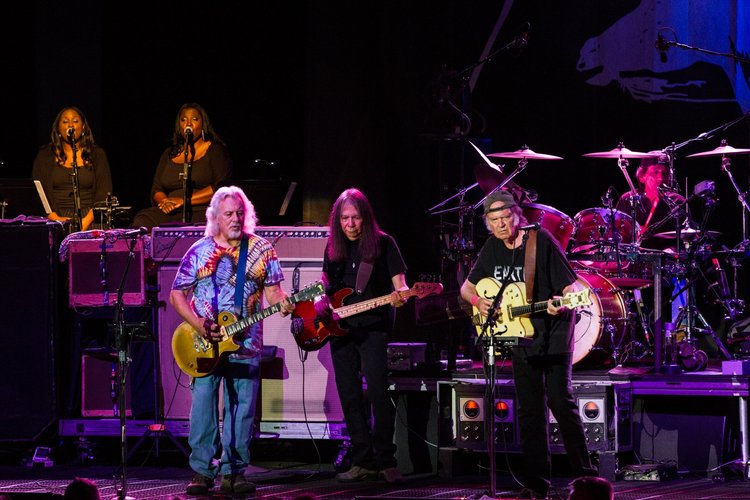 Music band performing on stage with guitarists, keyboardists, drummers, and backup singers during a concert.